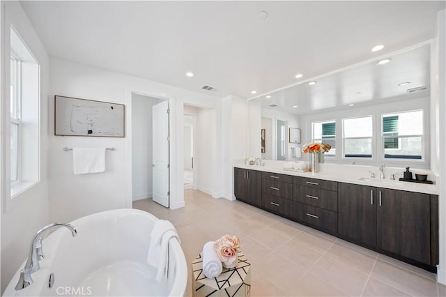 full bath featuring double vanity, a tub to relax in, a sink, and visible vents