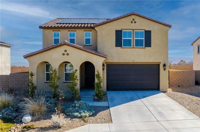 mediterranean / spanish home featuring a tile roof, stucco siding, concrete driveway, roof mounted solar panels, and fence