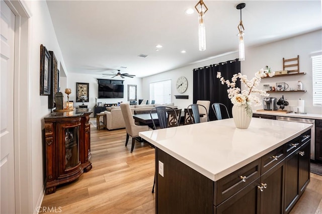 kitchen with a center island, a breakfast bar, pendant lighting, light countertops, and dark brown cabinets