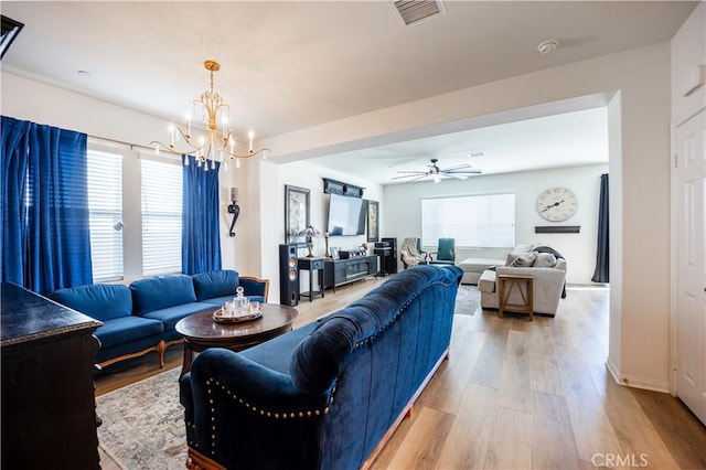 living room with light wood-style flooring, visible vents, a wealth of natural light, and ceiling fan with notable chandelier