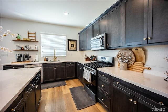 kitchen with open shelves, stainless steel appliances, light countertops, a sink, and light wood-type flooring