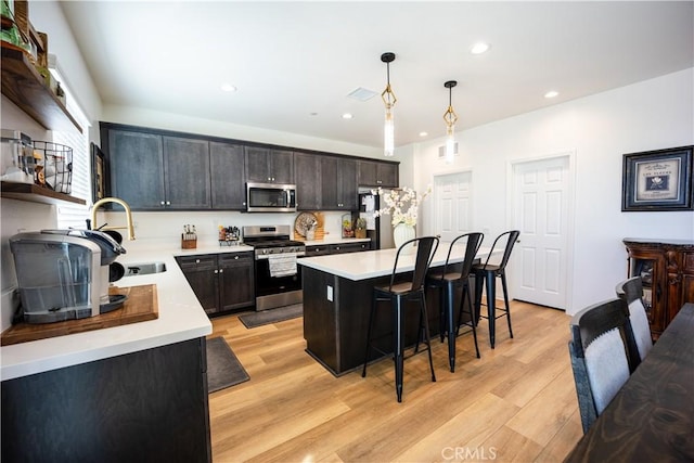 kitchen with stainless steel appliances, a sink, hanging light fixtures, light countertops, and a center island