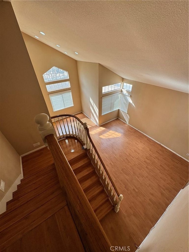 stairway featuring lofted ceiling, a textured ceiling, wood finished floors, and baseboards