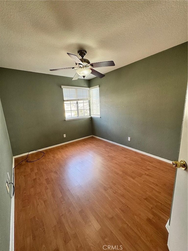 spare room with ceiling fan, a textured ceiling, baseboards, and wood finished floors