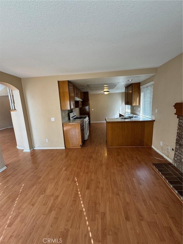 kitchen with brown cabinetry, open floor plan, wood finished floors, a peninsula, and white gas stove