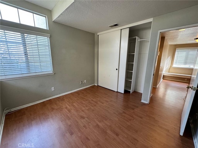 unfurnished bedroom featuring a textured ceiling, dark wood-type flooring, visible vents, and baseboards