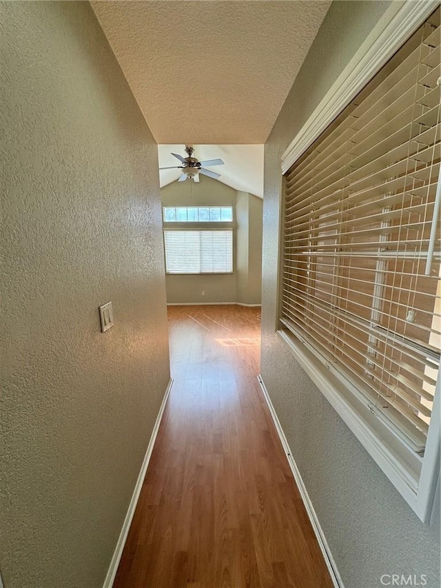 corridor with lofted ceiling, a textured wall, a textured ceiling, and wood finished floors