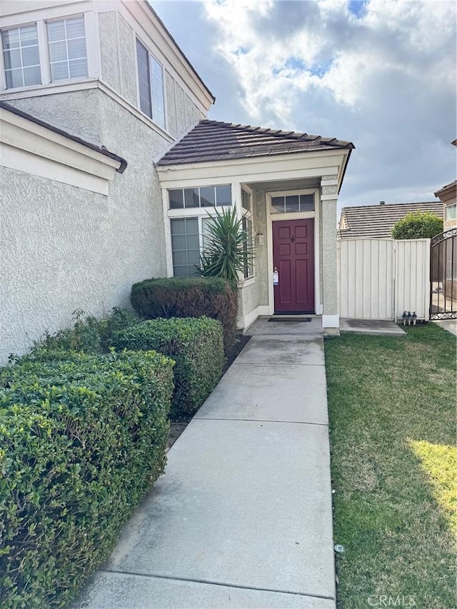 entrance to property with a lawn, fence, and stucco siding