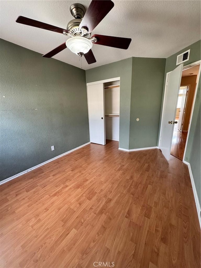 unfurnished bedroom with a closet, visible vents, a textured ceiling, wood finished floors, and baseboards