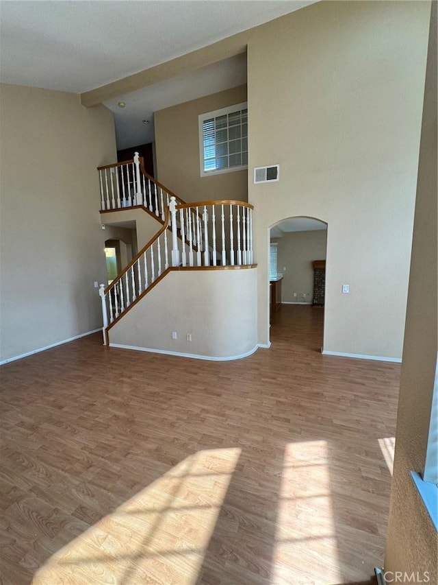 unfurnished living room featuring stairway, light wood-style flooring, visible vents, and arched walkways