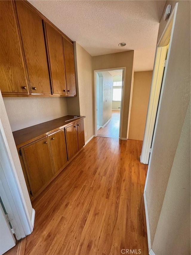 hallway with a textured ceiling, light wood-type flooring, and baseboards