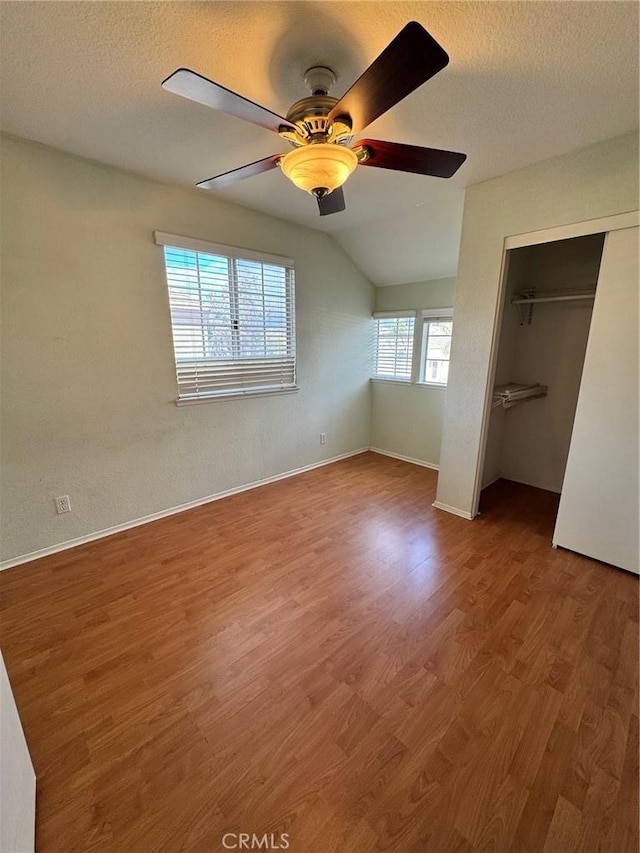 unfurnished bedroom with a closet, a ceiling fan, a textured ceiling, wood finished floors, and baseboards