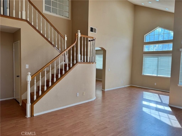 stairway featuring baseboards, visible vents, arched walkways, a towering ceiling, and wood finished floors