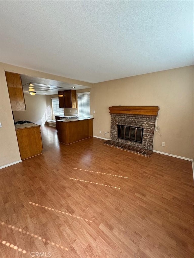 unfurnished living room featuring a brick fireplace, a textured ceiling, baseboards, and wood finished floors