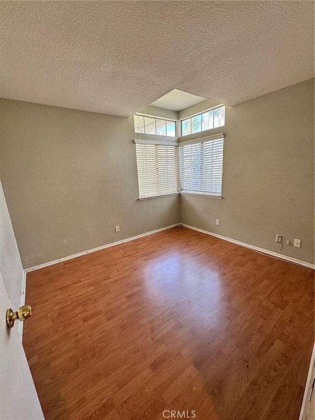 spare room with a textured ceiling, baseboards, and wood finished floors