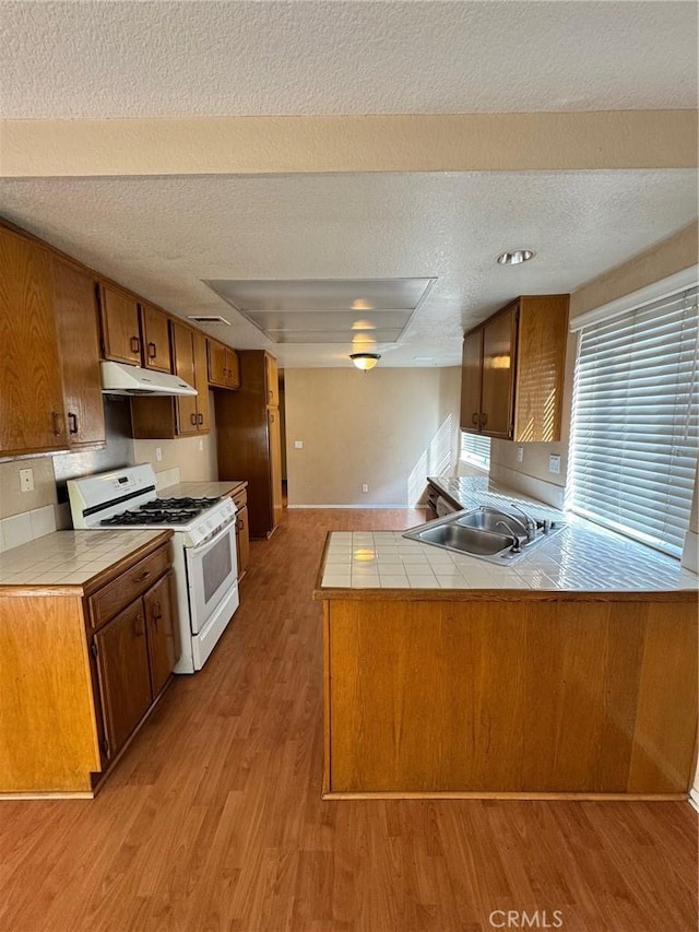 kitchen with under cabinet range hood, a peninsula, a sink, white gas range oven, and tile counters