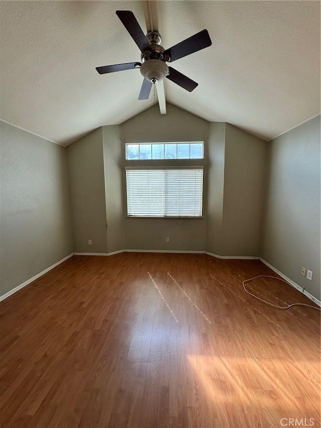 unfurnished room featuring vaulted ceiling, a textured ceiling, baseboards, and wood finished floors