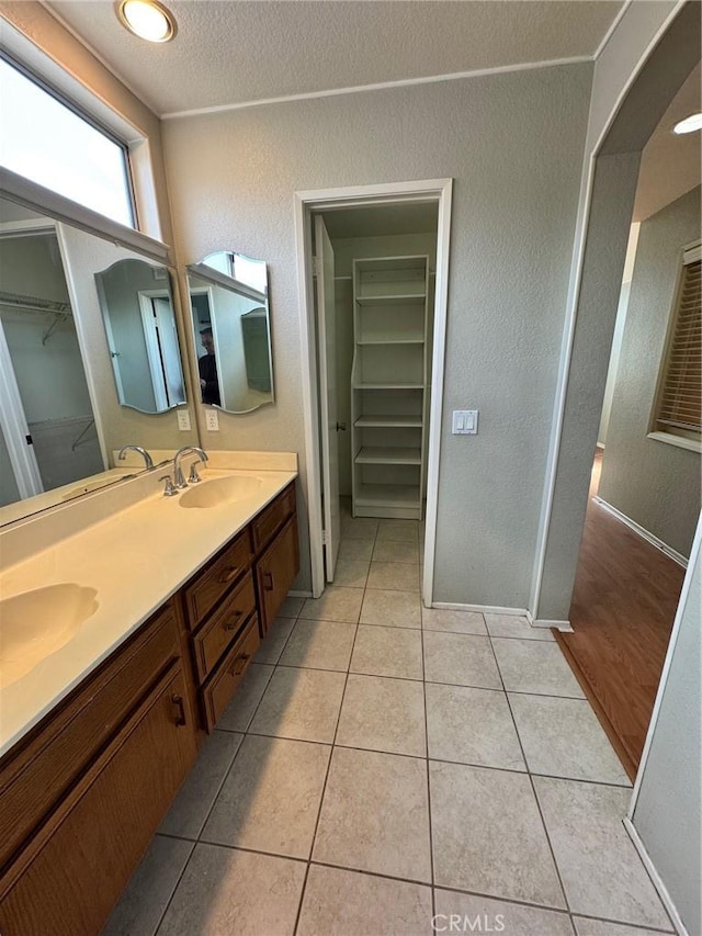 bathroom with a walk in closet, double vanity, a sink, and tile patterned floors