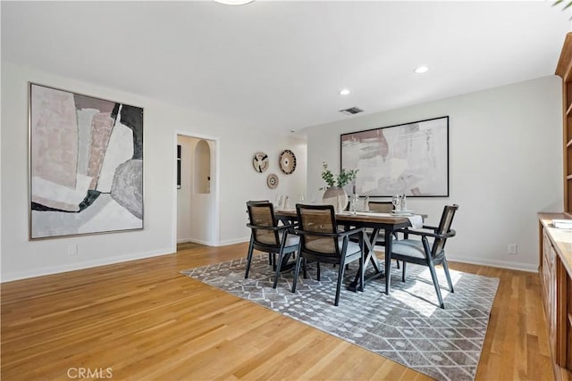 dining space featuring light wood-type flooring, baseboards, and arched walkways