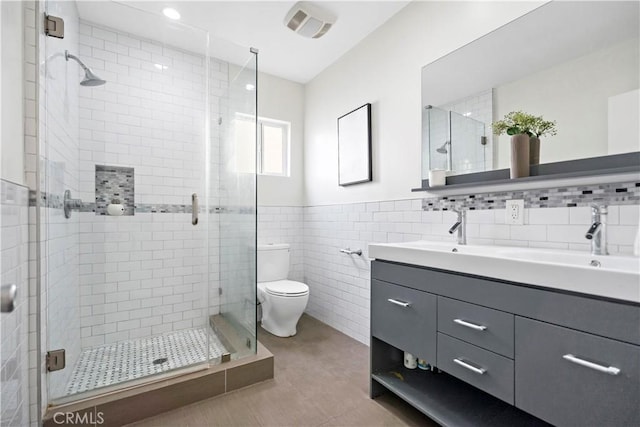 bathroom with double vanity, a stall shower, tile walls, and a sink