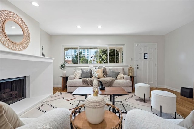 living room featuring a fireplace with raised hearth, baseboards, light wood-style flooring, and recessed lighting