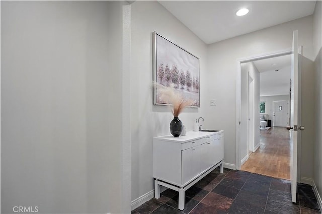 corridor with a sink, stone tile floors, and baseboards