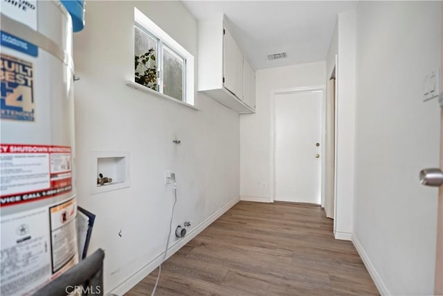 clothes washing area with strapped water heater, hookup for a washing machine, visible vents, wood finished floors, and baseboards