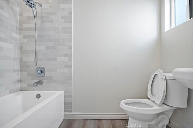 full bath with toilet, bathtub / shower combination, baseboards, and wood finished floors