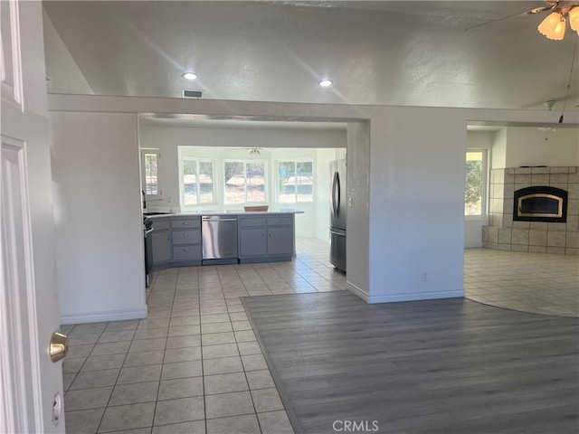 kitchen with light tile patterned floors, visible vents, ceiling fan, stainless steel appliances, and a fireplace