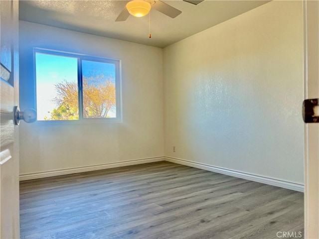 spare room with light wood-type flooring, ceiling fan, baseboards, and a textured ceiling