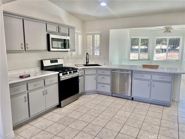 kitchen with appliances with stainless steel finishes, a peninsula, light countertops, gray cabinetry, and a sink