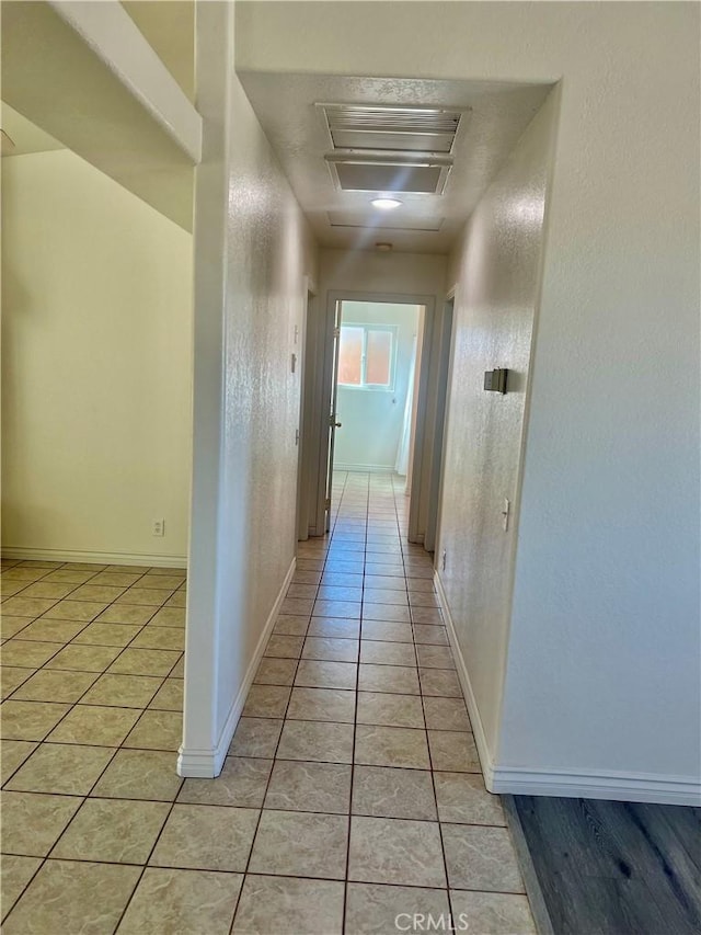 corridor featuring visible vents, baseboards, and light tile patterned floors