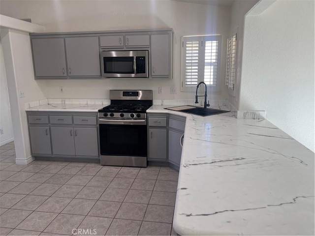 kitchen featuring appliances with stainless steel finishes, a sink, light stone counters, and gray cabinetry