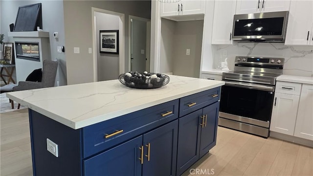 kitchen featuring blue cabinetry, appliances with stainless steel finishes, light wood-style floors, white cabinetry, and light stone countertops