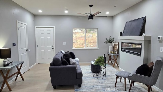 living area with light wood-type flooring, baseboards, a ceiling fan, and a glass covered fireplace