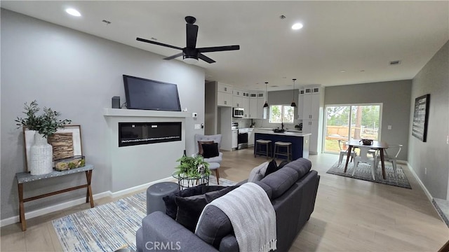 living area featuring baseboards, light wood finished floors, a glass covered fireplace, and recessed lighting