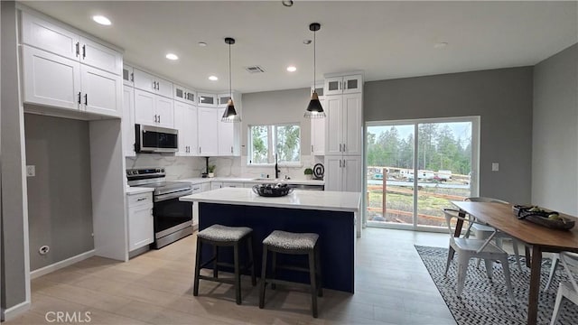 kitchen with light countertops, appliances with stainless steel finishes, glass insert cabinets, white cabinetry, and a kitchen island