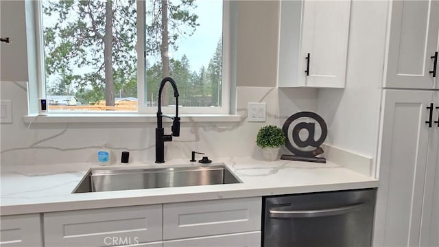 kitchen with a sink, light stone counters, white cabinets, and dishwasher