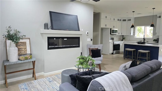 living room with ceiling fan, light wood-type flooring, a glass covered fireplace, and baseboards