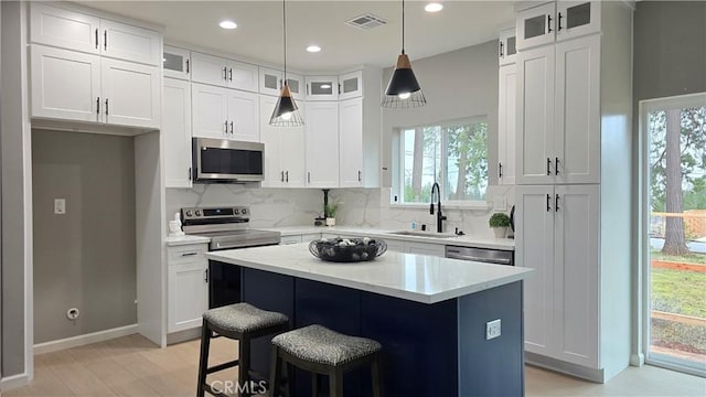 kitchen featuring a kitchen island, glass insert cabinets, appliances with stainless steel finishes, light countertops, and white cabinetry