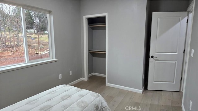 bedroom with multiple windows, a closet, light wood-style flooring, and baseboards