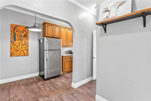 kitchen featuring arched walkways, decorative light fixtures, crown molding, brown cabinetry, and freestanding refrigerator