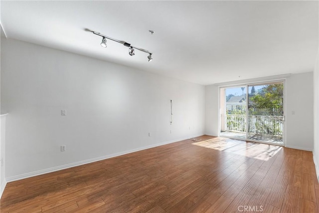 spare room with floor to ceiling windows, track lighting, wood finished floors, and baseboards