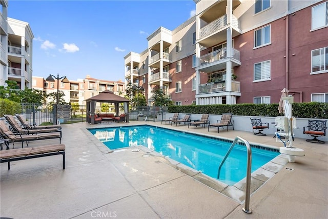 community pool with a patio area, fence, and a gazebo