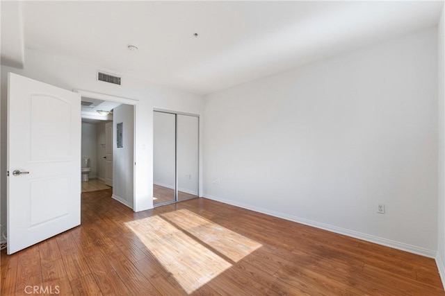 unfurnished bedroom featuring a closet, visible vents, baseboards, and wood finished floors