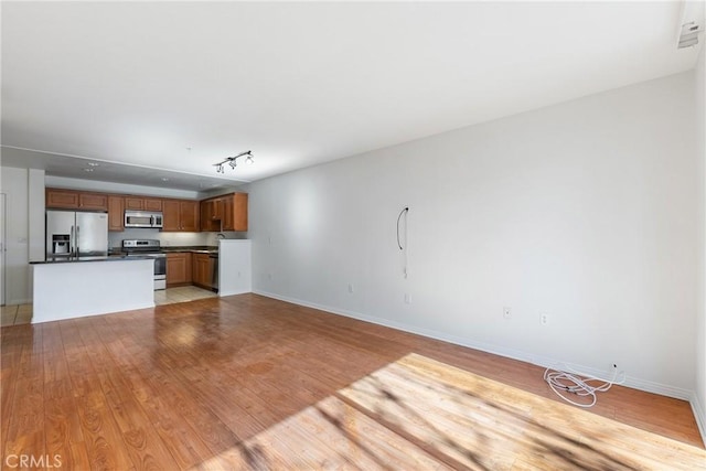 unfurnished living room featuring light wood finished floors, a sink, rail lighting, and baseboards