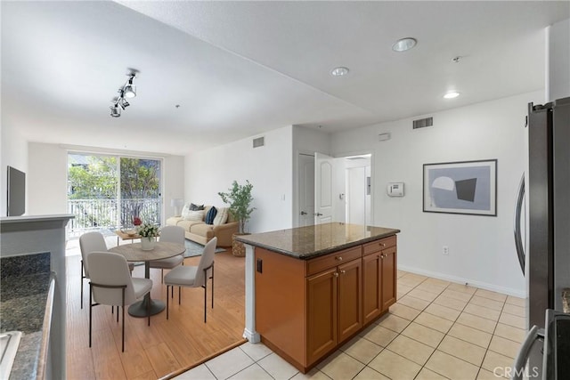 kitchen with baseboards, dark stone counters, visible vents, brown cabinets, and freestanding refrigerator