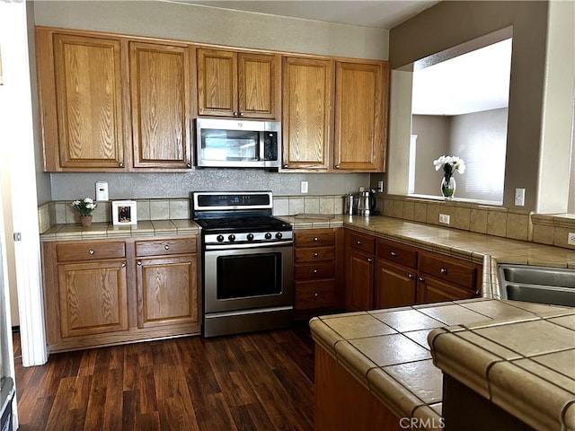 kitchen with stainless steel appliances, dark wood-type flooring, a sink, tile counters, and brown cabinets