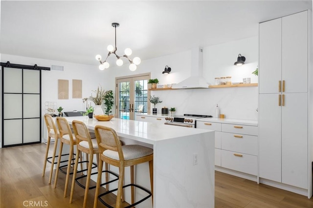 kitchen featuring wall chimney range hood, open shelves, modern cabinets, light wood finished floors, and white cabinetry