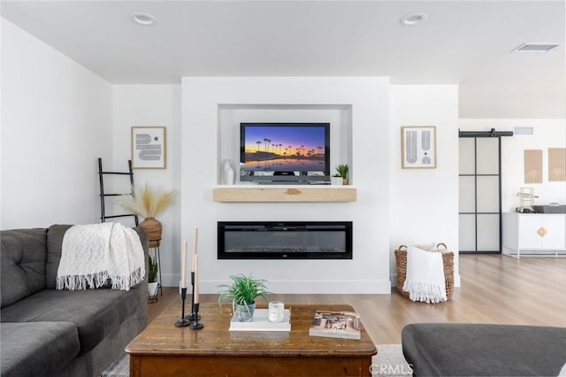 living area with visible vents, a barn door, a glass covered fireplace, recessed lighting, and wood finished floors